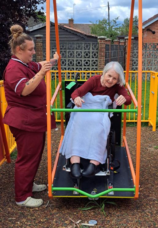 A female carer with a female resident in a wheel chair using an accessible swing in a park.