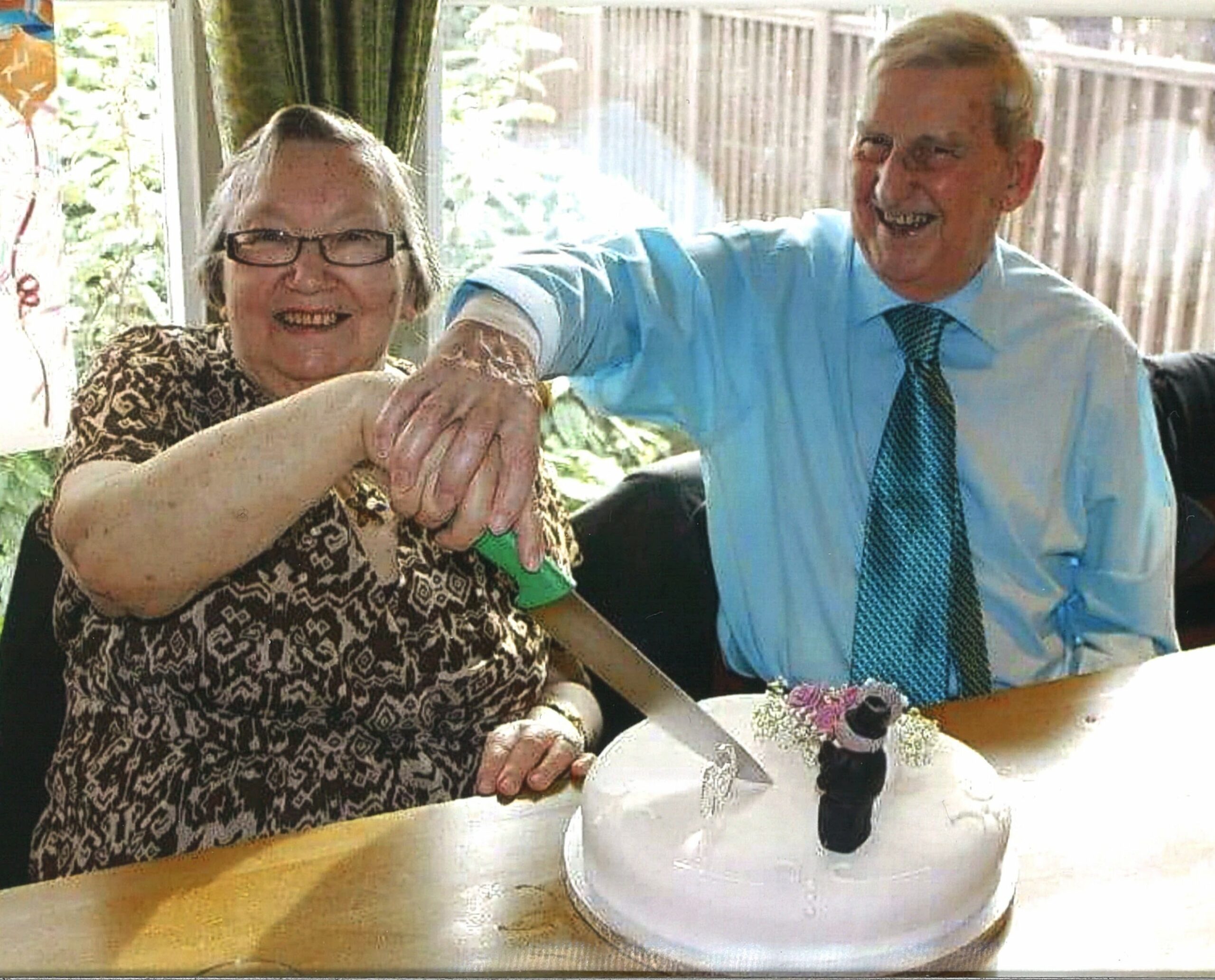 Two smiling residents cutting into a wedding anniversary cake.