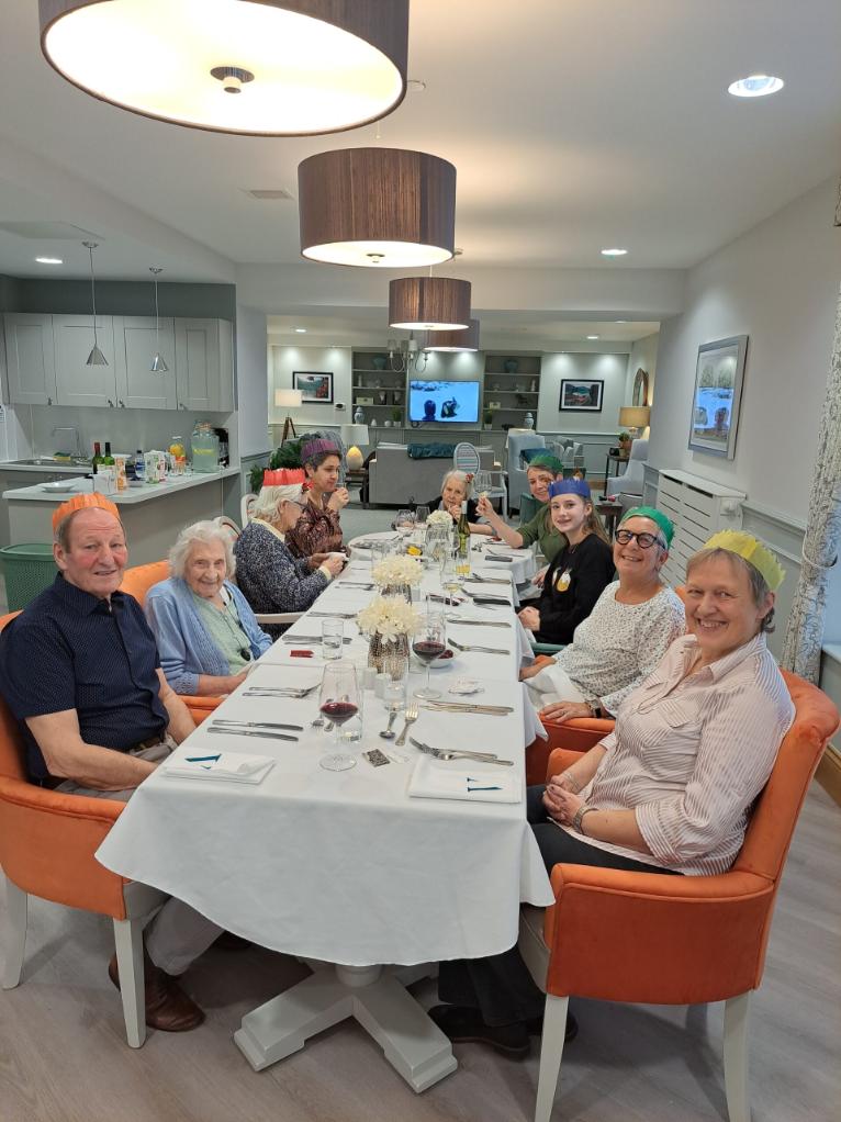 Residents and loved one with Christmas hats around a dinner table.