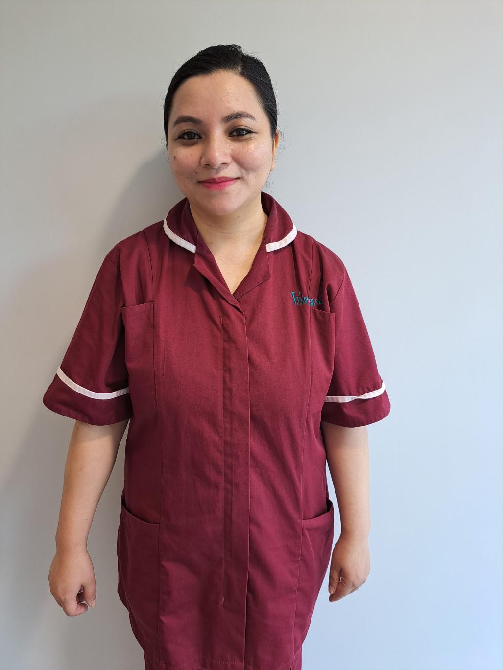 A female carer with her hair up and in a dark red uniform.