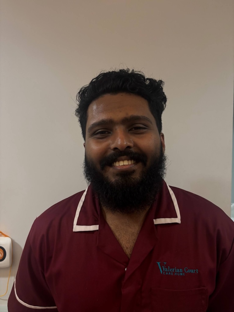 Man with black hair smiling wearing a red carers uniform