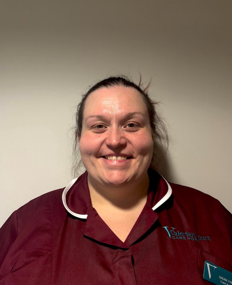 woman with brown hair tied back smiling with a red carers uniform on having a headshot for the team page