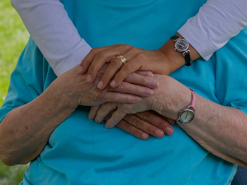 someone with a purple top holding their hands over someone in a wheelchair wearing a blue top in support