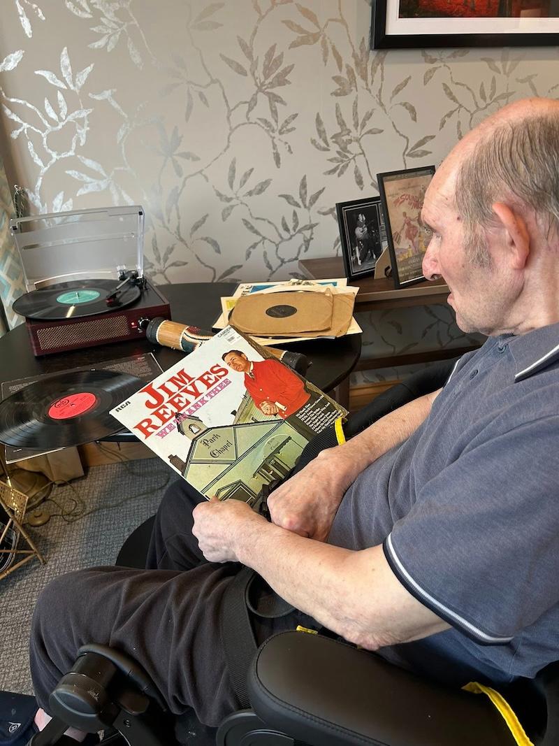 elderly man sat in a wheelchair holding a jim reeves vynyl case
