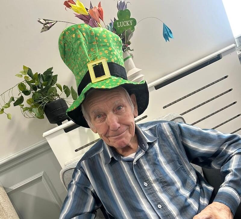 male resident sat down in an armchair smiling wearing a green st patricks day hat