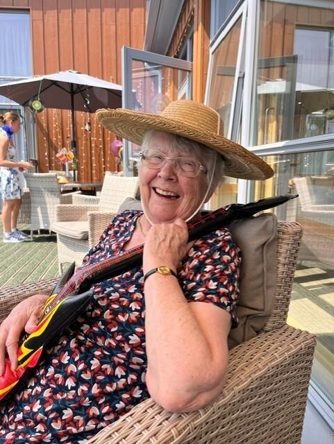 older lady in a hat holding an inflatable guitar